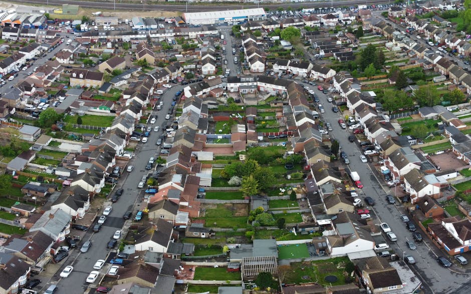 An aerial black-and-white photograph of a residential area featuring a variety of gardens, lawns, and pathways among rows of terraced and semi-detached houses. In the foreground, there are back garden